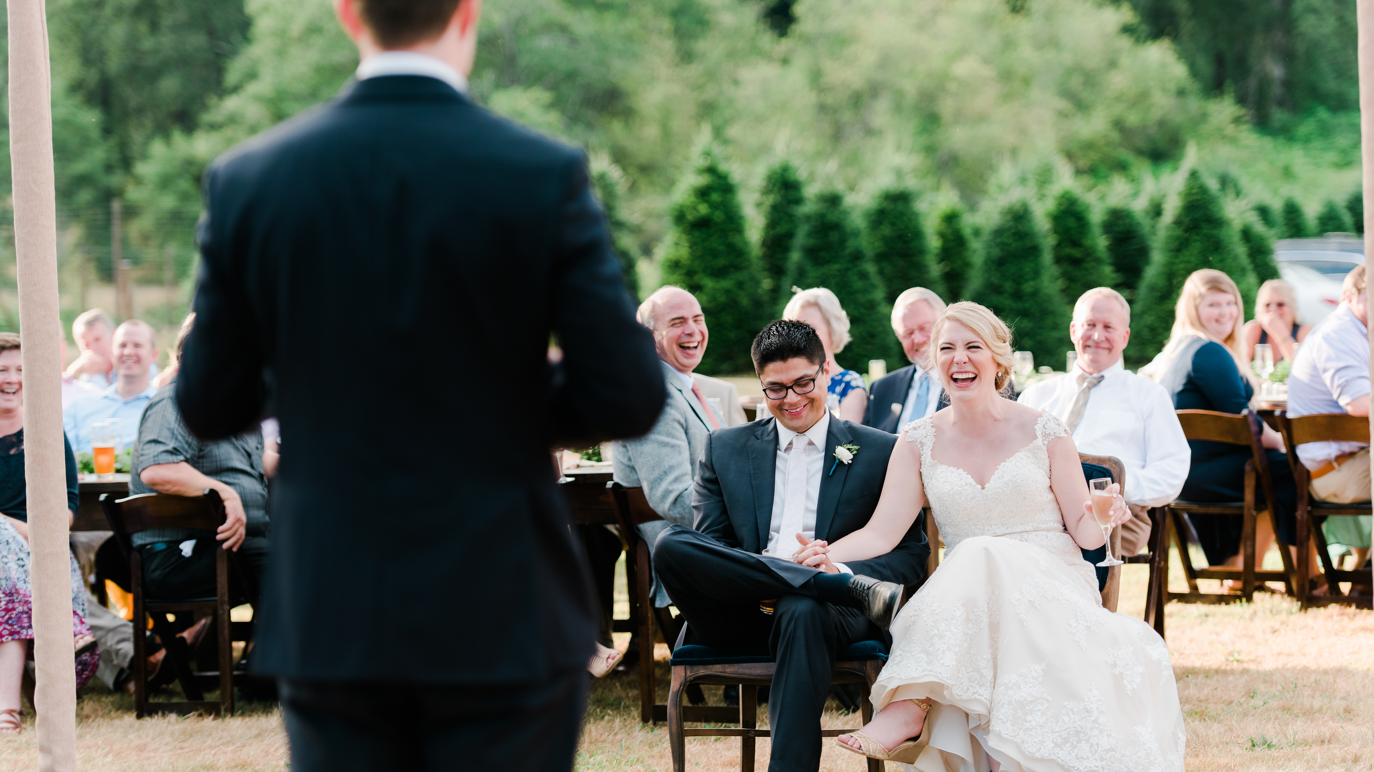 Bride and groom laughing at man giving a wedding speech